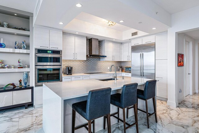 kitchen featuring light tile patterned floors, wall chimney range hood, appliances with stainless steel finishes, decorative backsplash, and sink