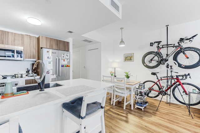 kitchen featuring pendant lighting, light hardwood / wood-style flooring, stainless steel appliances, and a kitchen breakfast bar