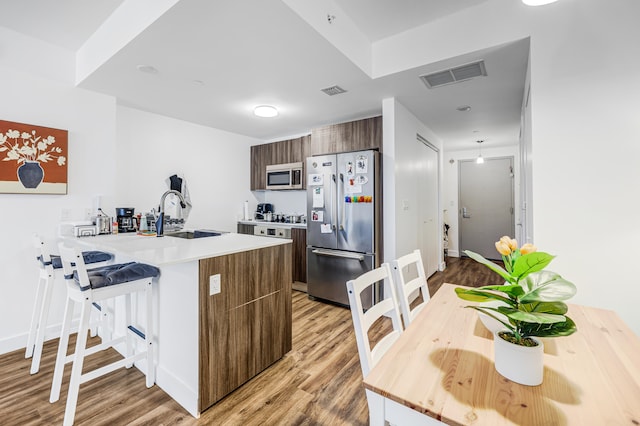 kitchen with light wood-type flooring, stainless steel appliances, sink, kitchen peninsula, and a kitchen breakfast bar