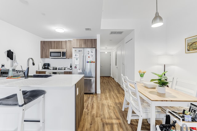 kitchen featuring a kitchen breakfast bar, pendant lighting, appliances with stainless steel finishes, light hardwood / wood-style floors, and sink