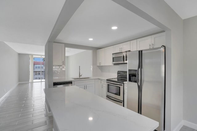 kitchen featuring white cabinets, stainless steel appliances, light stone counters, and sink