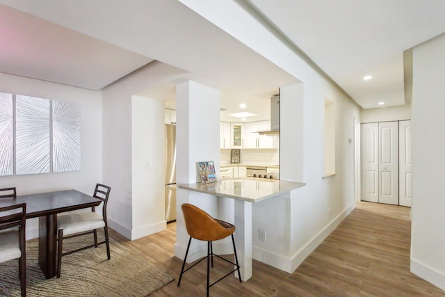 kitchen with stainless steel appliances, kitchen peninsula, decorative backsplash, light wood-type flooring, and white cabinetry