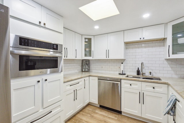 kitchen featuring white cabinetry, light hardwood / wood-style flooring, backsplash, light stone counters, and stainless steel appliances