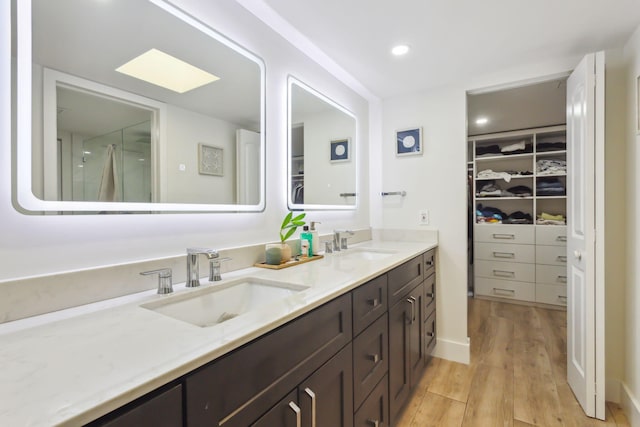 bathroom with a walk in closet, double vanity, a sink, and wood finished floors