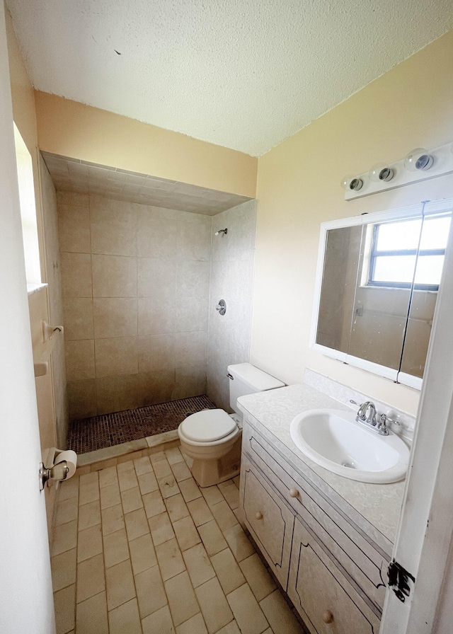 bathroom featuring a textured ceiling, tiled shower, toilet, vanity, and tile patterned flooring