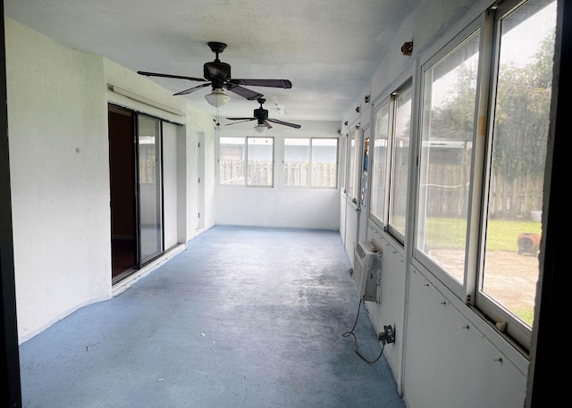 unfurnished sunroom with ceiling fan and a wall mounted AC