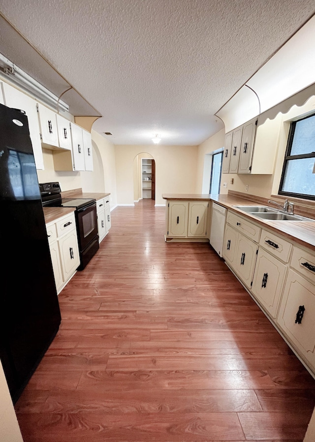 kitchen featuring light wood-type flooring, a textured ceiling, black appliances, sink, and kitchen peninsula