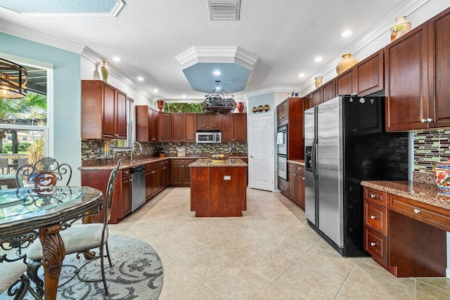 kitchen with appliances with stainless steel finishes, a textured ceiling, backsplash, crown molding, and a kitchen island