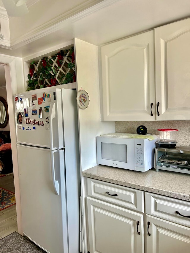 kitchen with white cabinetry, ornamental molding, white appliances, and tile patterned floors