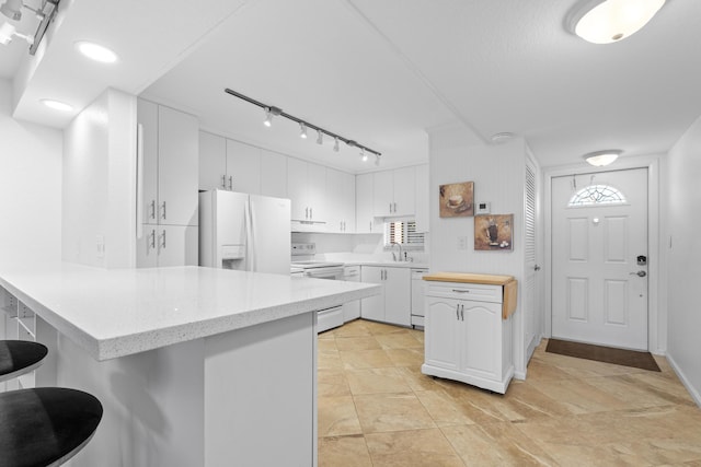 kitchen featuring a peninsula, white appliances, a sink, white cabinets, and a kitchen bar