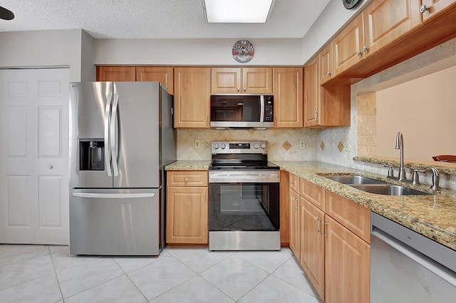 kitchen with backsplash, light stone counters, sink, and stainless steel appliances