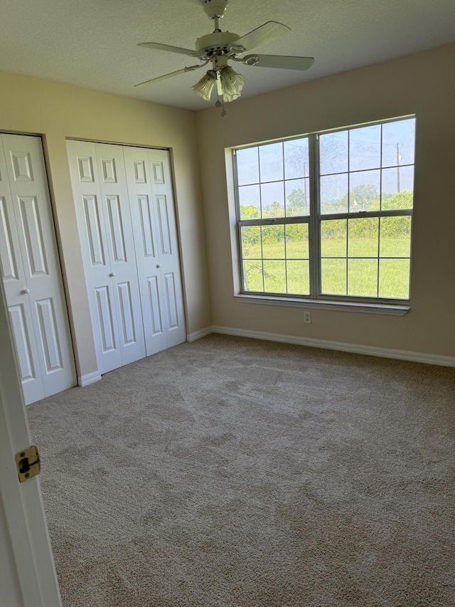 unfurnished bedroom with ceiling fan, multiple closets, and carpet floors