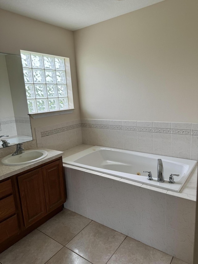 bathroom featuring tile patterned flooring, tiled tub, vanity, and a textured ceiling