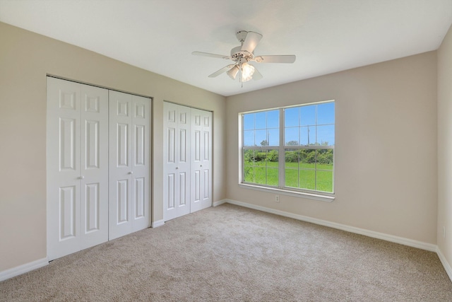 unfurnished bedroom featuring ceiling fan, multiple closets, and light colored carpet