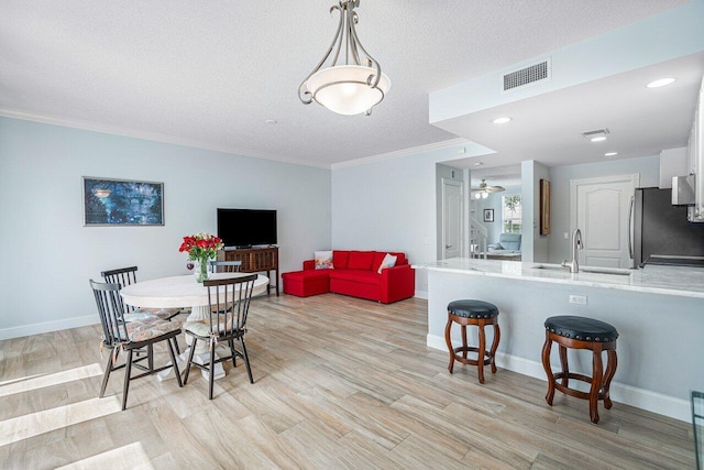 dining area featuring a textured ceiling, light hardwood / wood-style floors, ornamental molding, and sink