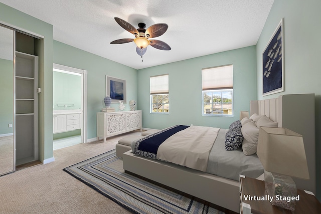 carpeted bedroom with a textured ceiling, ceiling fan, ensuite bath, and baseboards