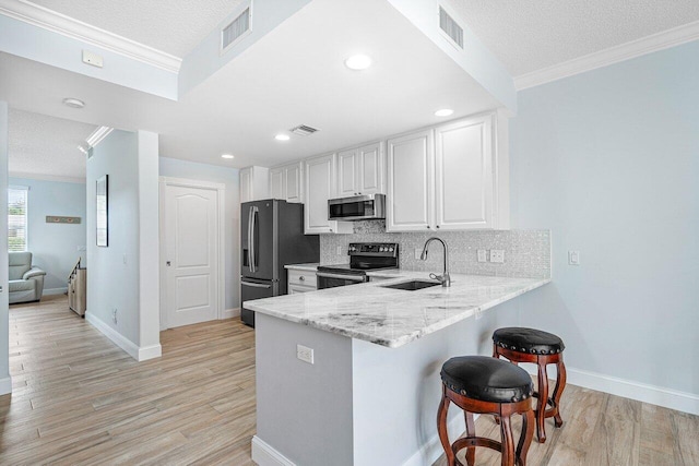 kitchen featuring sink, appliances with stainless steel finishes, a textured ceiling, white cabinets, and light wood-type flooring