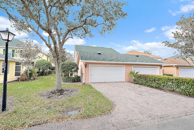 view of front of home featuring an attached garage, roof with shingles, decorative driveway, stucco siding, and a front lawn