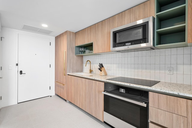 kitchen with sink, tasteful backsplash, light stone countertops, black appliances, and light brown cabinetry