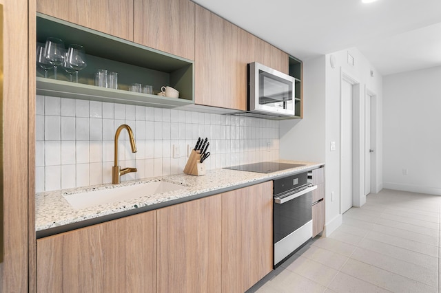 kitchen with sink, stainless steel appliances, light stone counters, light tile patterned flooring, and decorative backsplash