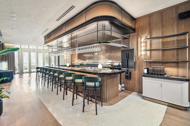 bar featuring light hardwood / wood-style floors, white cabinets, a wall of windows, and wood walls