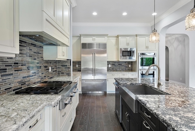 kitchen featuring decorative backsplash, built in appliances, pendant lighting, dark wood-type flooring, and crown molding