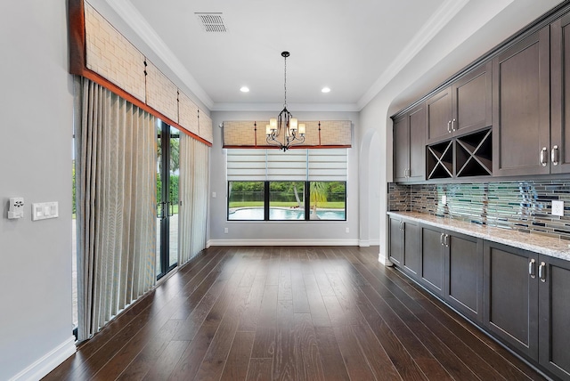 kitchen featuring decorative light fixtures, tasteful backsplash, light stone counters, crown molding, and dark wood-type flooring