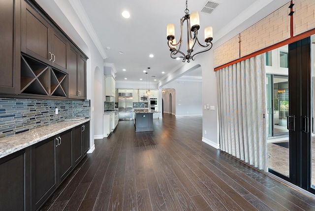 kitchen featuring dark wood-type flooring, ornamental molding, light stone countertops, and hanging light fixtures