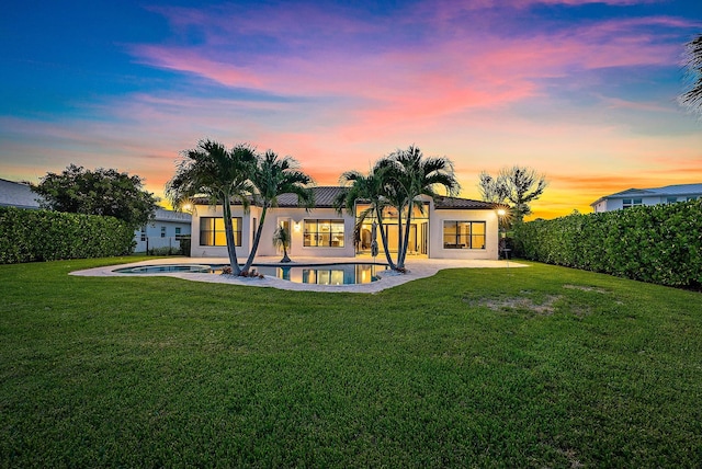 back house at dusk with a lawn and a fenced in pool