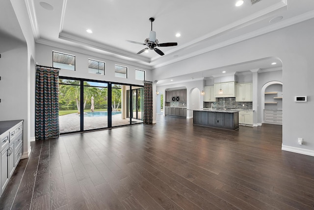 unfurnished living room featuring dark hardwood / wood-style flooring, ornamental molding, a raised ceiling, and ceiling fan