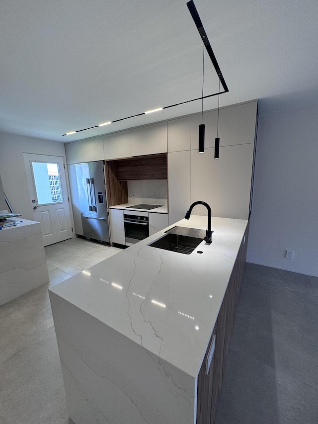 kitchen featuring high end fridge, modern cabinets, a sink, light stone countertops, and oven