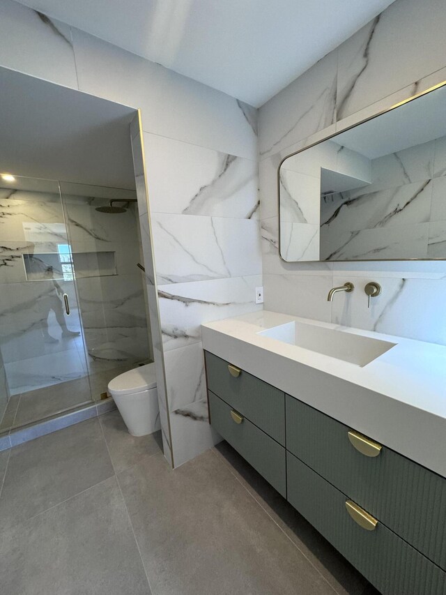 bathroom with a shower with door, toilet, vanity, tile patterned floors, and tile walls