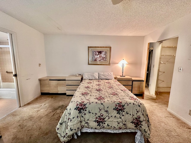 carpeted bedroom with a spacious closet, ensuite bath, a closet, and a textured ceiling