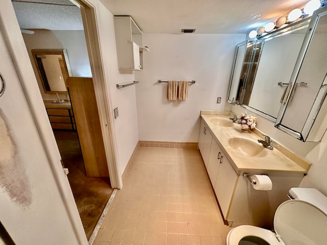 bathroom with vanity, toilet, a textured ceiling, and tile patterned floors