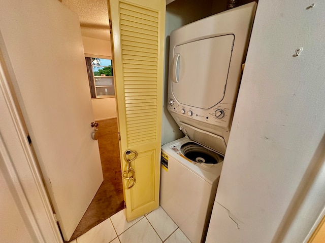 clothes washing area with a textured ceiling, stacked washer / dryer, and light tile patterned floors