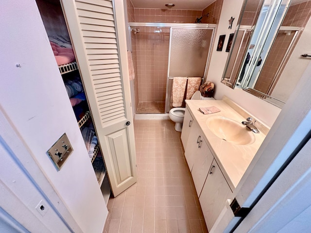 bathroom featuring tile patterned flooring, vanity, toilet, and a shower with shower door