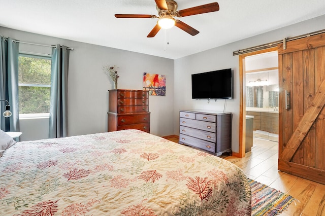 bedroom with a barn door, connected bathroom, ceiling fan, and light hardwood / wood-style flooring