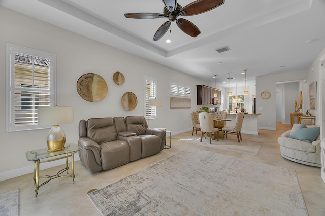 living room featuring a raised ceiling, light tile patterned floors, and ceiling fan