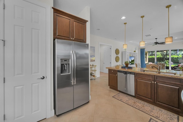 kitchen featuring ceiling fan, stainless steel appliances, pendant lighting, sink, and light stone countertops