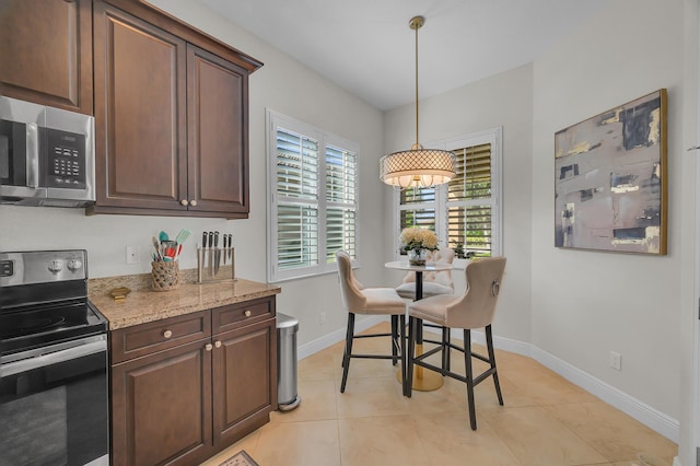 kitchen with light tile patterned floors, light stone counters, hanging light fixtures, appliances with stainless steel finishes, and dark brown cabinetry