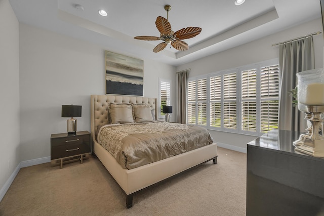 bedroom with light colored carpet, a raised ceiling, and ceiling fan