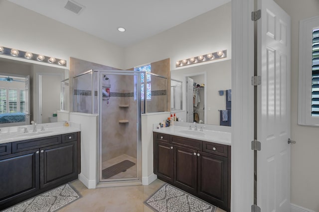 bathroom with tile patterned floors, dual vanity, a shower with shower door, and ceiling fan