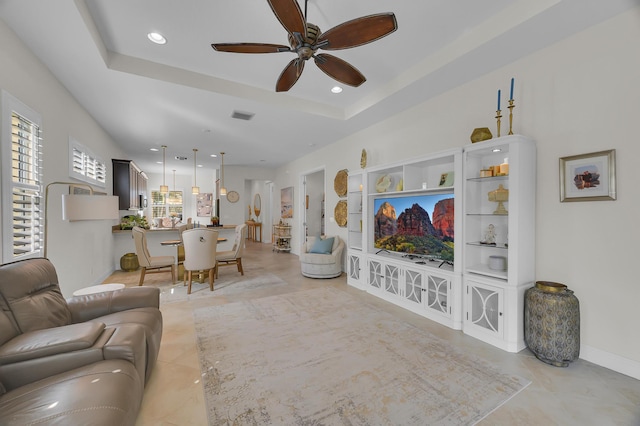 tiled living room with ceiling fan and a tray ceiling