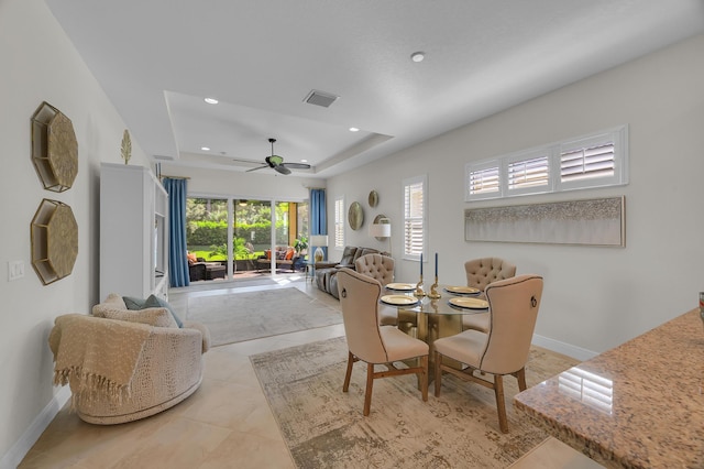 tiled dining area with ceiling fan and a tray ceiling