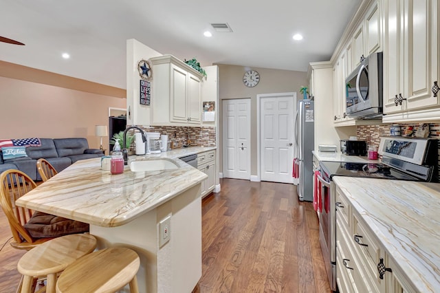 kitchen featuring tasteful backsplash, stainless steel appliances, sink, a kitchen breakfast bar, and dark wood-type flooring