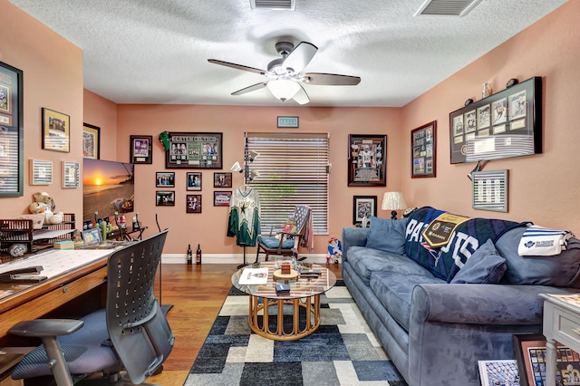 living room with a textured ceiling, wood-type flooring, and ceiling fan