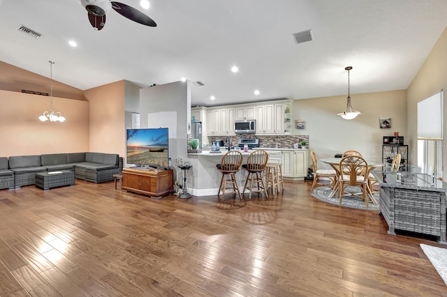 living room with light wood-type flooring, ceiling fan with notable chandelier, and vaulted ceiling