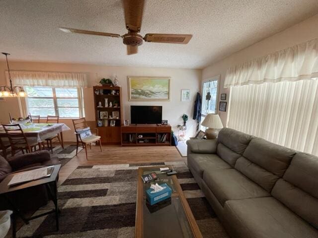 living room featuring a textured ceiling, ceiling fan with notable chandelier, and wood-type flooring