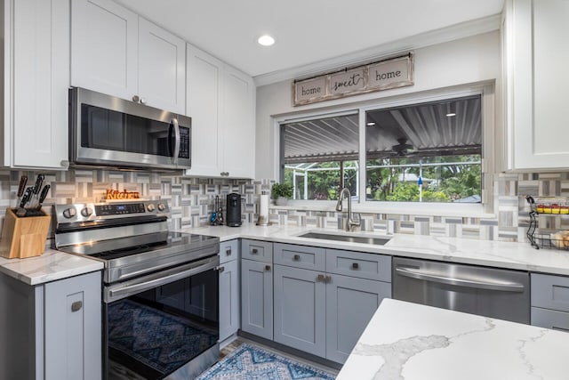 kitchen with light stone counters, appliances with stainless steel finishes, gray cabinetry, backsplash, and sink