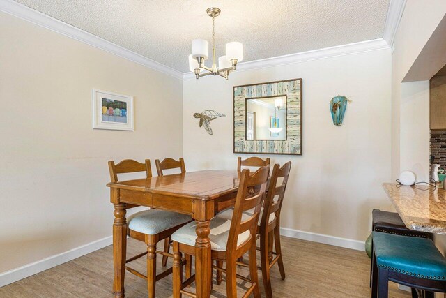 dining area featuring light wood-type flooring, a notable chandelier, ornamental molding, and a textured ceiling